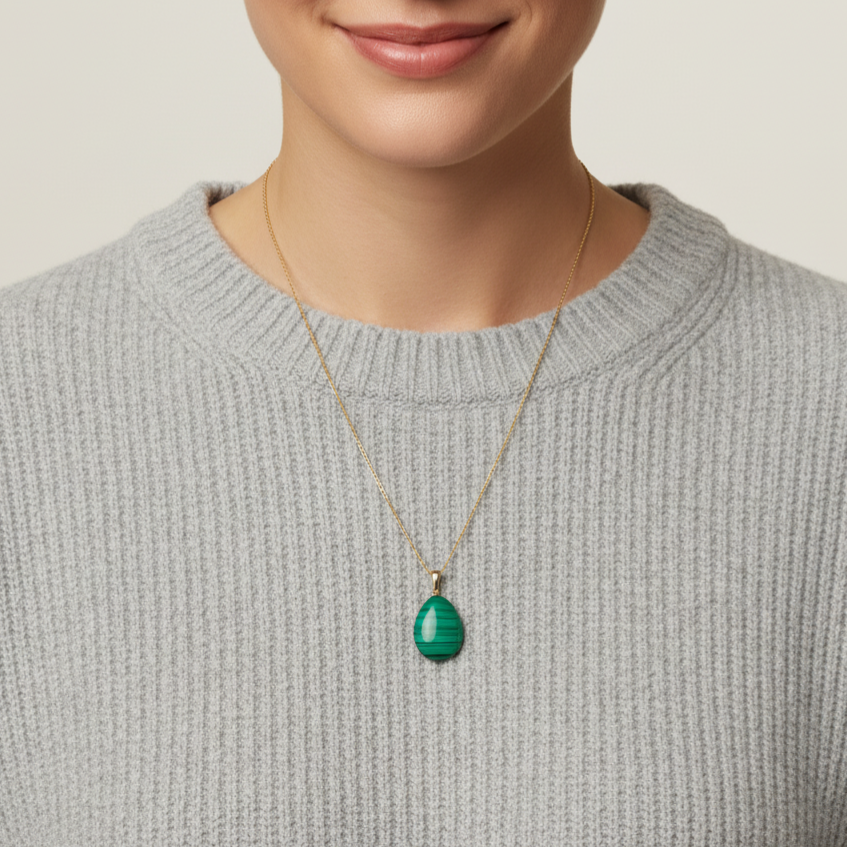 Eine Frau mit grauem Wollpullover und einer Halskette aus 585 Gold und einem Edelsteinanhänger aus Malachit als glatte Briolette Form 29mm