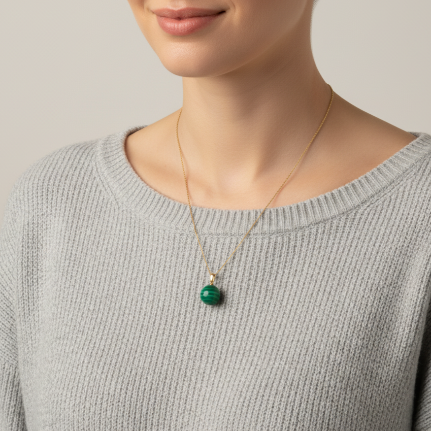 Eine Frau mit grauem Wollpullover trägt eine Halskette aus 585 Gold und einen Edelsteinanhänger mit Malachit in Kugelform